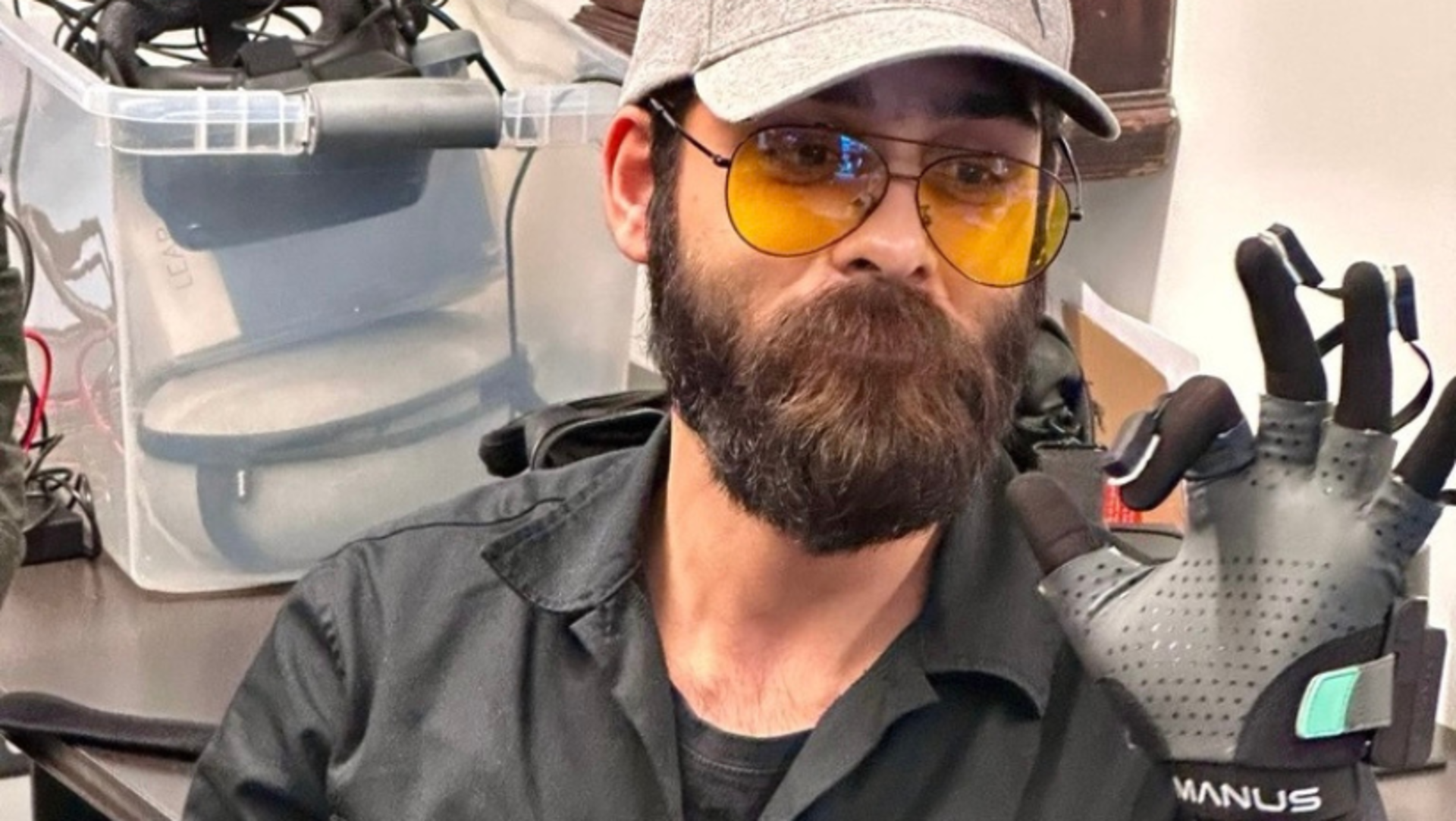 Man with beard and yellow glasses showing a black Manus VR glove.