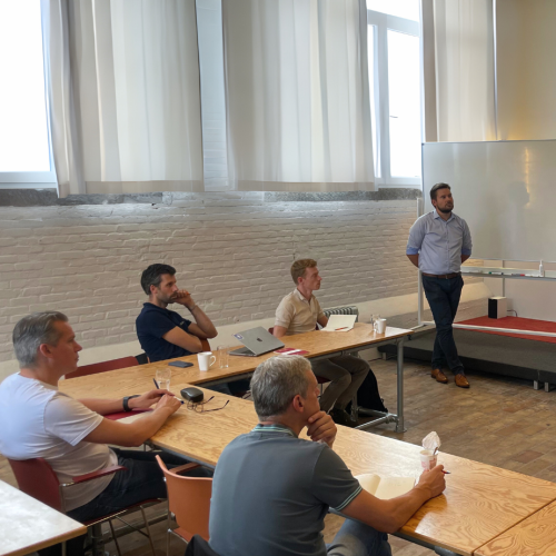 People working at standing and sitting desks in a modern office with large windows.