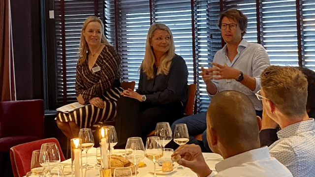Three people (two women, one man) seated in a restaurant, actively conversing while others dine.