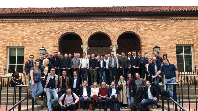 Group of professionals posing on steps in front of a brick building with arched entryways.